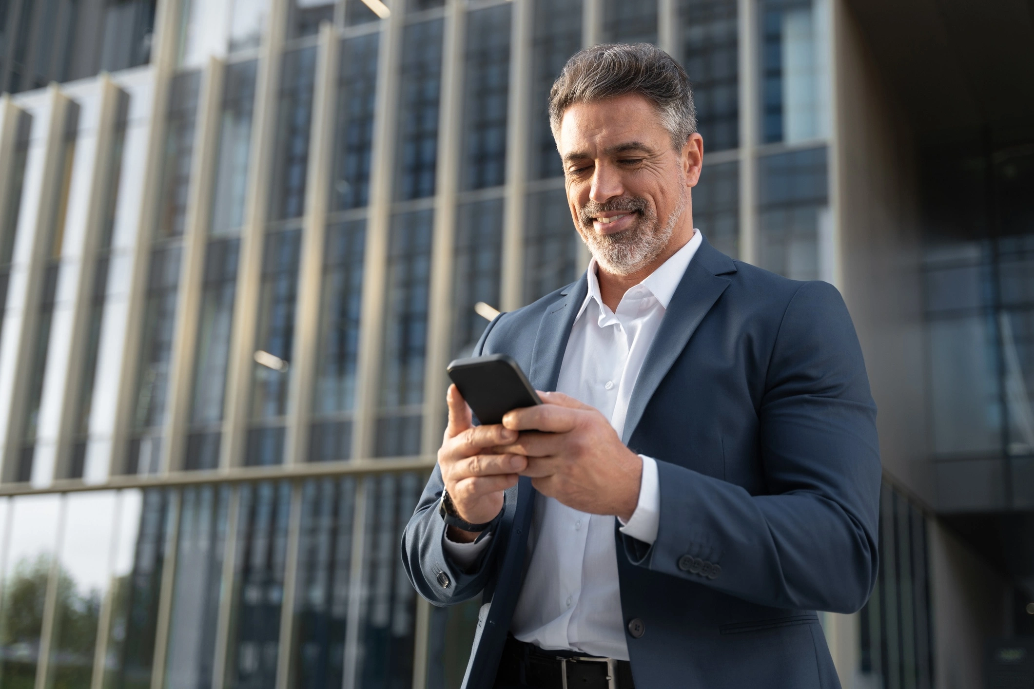 executive walking out of office building, looking at phone and smiling