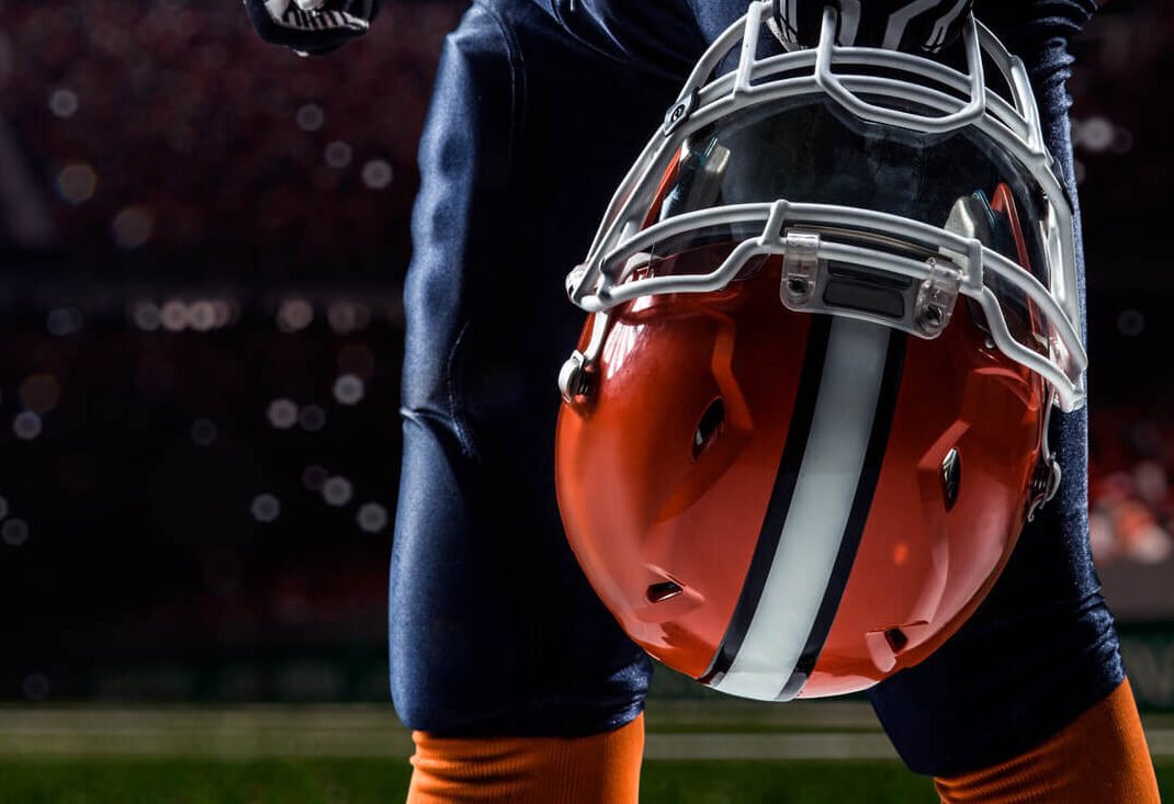 professional football player in stadium, carrying his helmet in hand