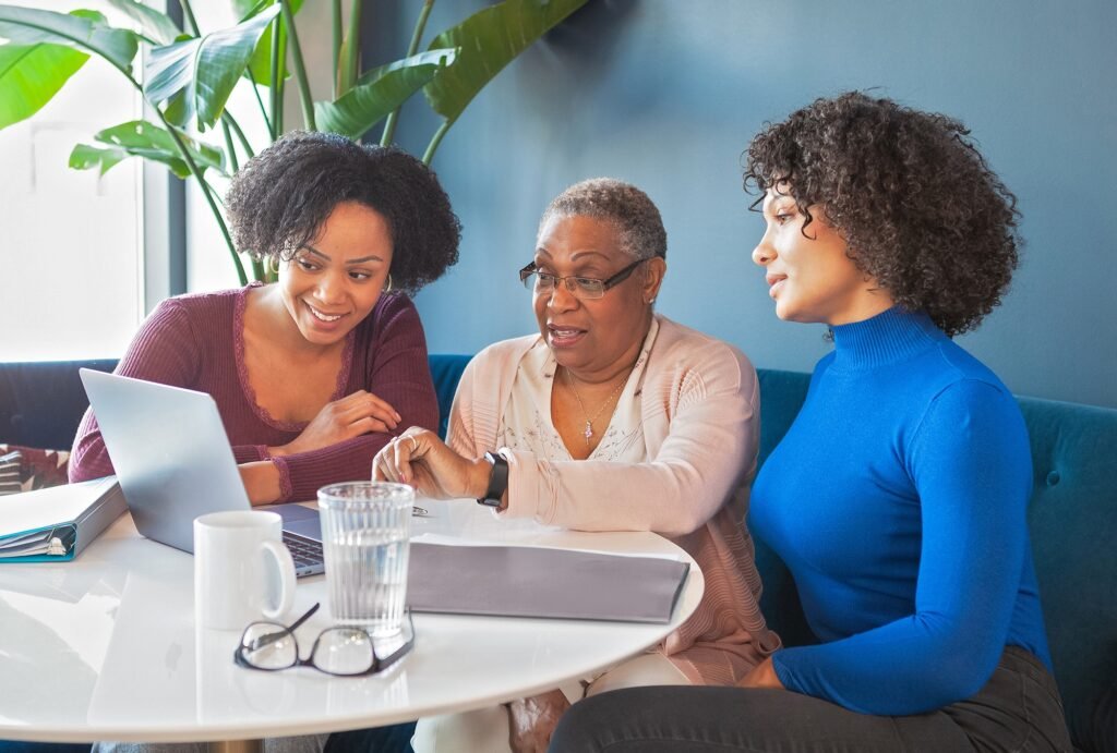 multiple generations within a family (grandmother, mother and daughter) sitting at a table looking at computer and financial statements